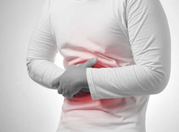A person wearing a white shirt holds their stomach with both hands, showing discomfort or pain possibly caused by arsenic in water. The abdominal area is highlighted in red to indicate pain or illness.