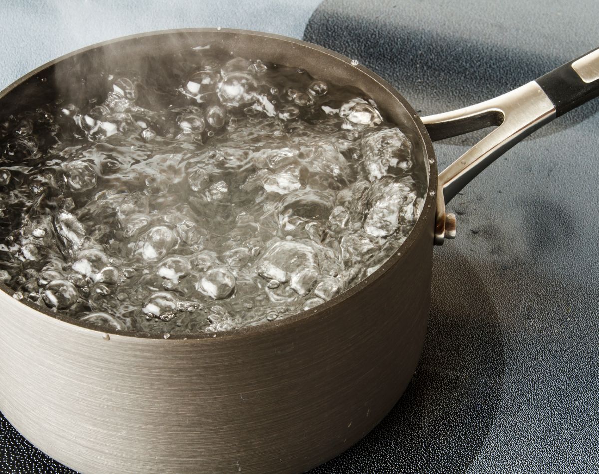 A metal pot filled with rapidly boiling water sits on a stovetop, steam rising above the bubbling surface—showcasing the purity achieved by whole home water treatment systems.