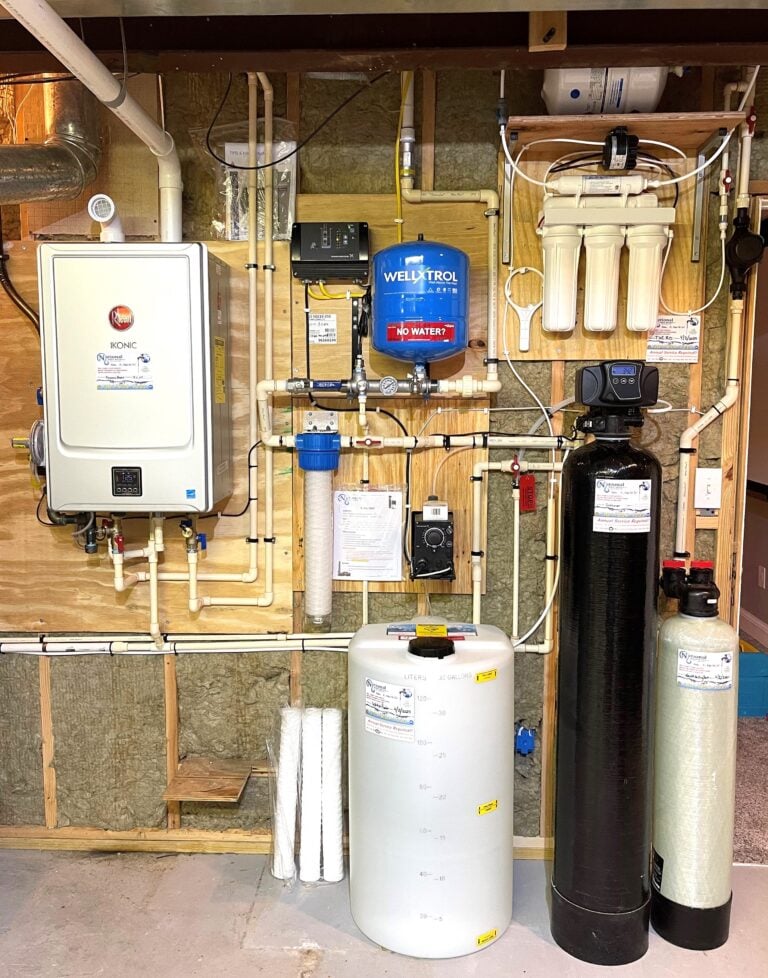 A home water filtration and softener system, expertly installed by a national water service, mounted on unfinished wooden basement walls with tanks, filters, pipes, a control panel, and a blue Wellxtrol pressure tank for seamless plumbing.