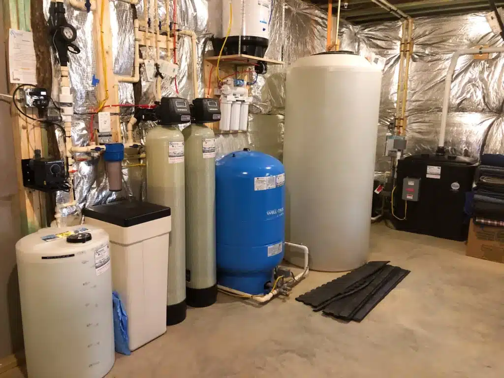 A Maryland Water Treatment system featuring large tanks, a blue pressure tank, water filtration units, and pipes is installed against a wall with reflective insulation. The concrete floor remains clear and clean.