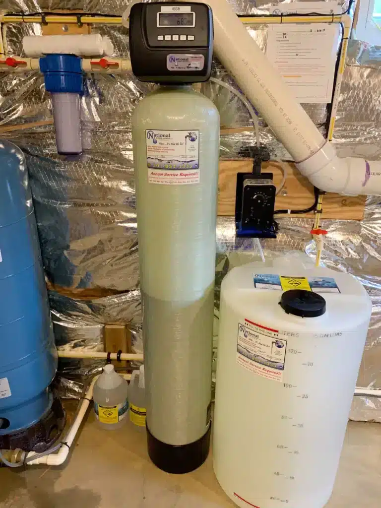 A water softener system with a tall fiberglass tank, digital control head, white brine tank, and pipes is installed in a Maryland basement with foil-covered insulation on the walls—perfect for homes needing reliable water testing.