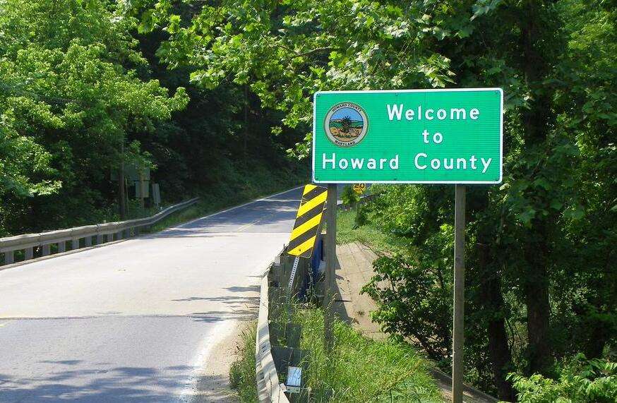 A green roadside sign reads Welcome to Howard County beside a two-lane road bordered by trees and greenery, highlighting a community known for its commitment to environmental stewardship and advanced Howard County water treatment.