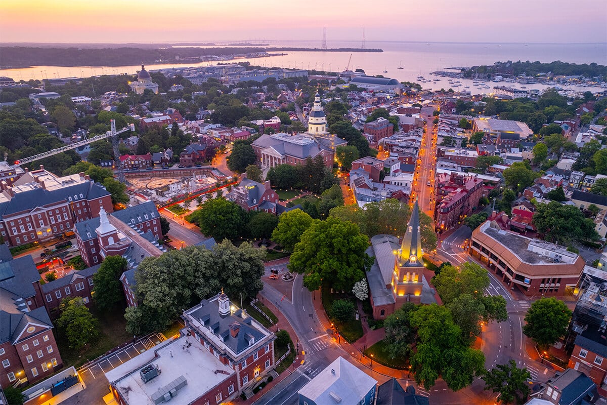 Aerial view of a historic coastal city at sunset, featuring tree-lined streets, red-brick buildings, a domed capitol building, and a harbor with boats—set within Anne Arundel County, known for its advanced water treatment facilities.
