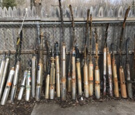 A row of old, rusted and weathered metal submersible pumps, some with attached cables, leaning upright against a chain-link fence forms a unique display reminiscent of a National Water Service gallery. A row of old, rusted and weathered metal submersible pumps, some with attached cables, leaning upright against a chain-link fence forms a unique display reminiscent of a National Water Service gallery.