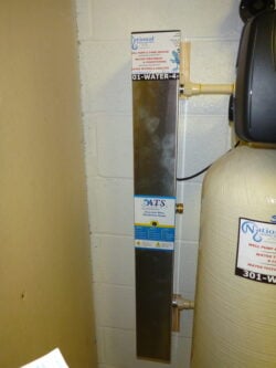 Tall, rectangular metal gauge attached to a wall next to a large cylindrical water treatment tank; labels for National Water and ATS are visible at the top and center of the gauge. Tall, rectangular metal gauge attached to a wall next to a large cylindrical water treatment tank; labels for National Water and ATS are visible at the top and center of the gauge.