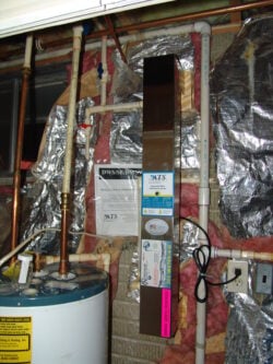 A basement utility area with exposed pipes, insulation, a water heater, and an upright stainless steel UV water purification system mounted on the wall. A power outlet and electrical cords are visible nearby. A basement utility area with exposed pipes, insulation, a water heater, and an upright stainless steel UV water purification system mounted on the wall. A power outlet and electrical cords are visible nearby.