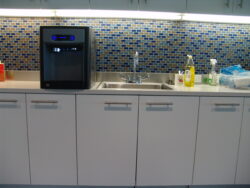 A modern kitchen counter with white cabinets, a sink, a black appliance, cleaning supplies, and a blue and white mosaic tile backsplash. A modern kitchen counter with white cabinets, a sink, a black appliance, cleaning supplies, and a blue and white mosaic tile backsplash.