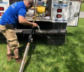 A worker in a blue shirt and khaki shorts handles well pump equipment at the back of a service truck labeled “Emergency Well Pump Service” on a grassy lawn. Tools and coiled hoses are visible on the truck. A worker in a blue shirt and khaki shorts handles well pump equipment at the back of a service truck labeled “Emergency Well Pump Service” on a grassy lawn. Tools and coiled hoses are visible on the truck.