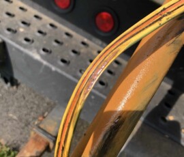 Close-up of a yellow hydraulic hose with visible damage, showing exposed inner layers, positioned against metal machinery with red lights and perforated metal in the background. Close-up of a yellow hydraulic hose with visible damage, showing exposed inner layers, positioned against metal machinery with red lights and perforated metal in the background.