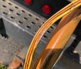 Close-up of a yellow hydraulic hose with visible damage, showing exposed inner layers, positioned against metal machinery with red lights and perforated metal in the background. Close-up of a yellow hydraulic hose with visible damage, showing exposed inner layers, positioned against metal machinery with red lights and perforated metal in the background.