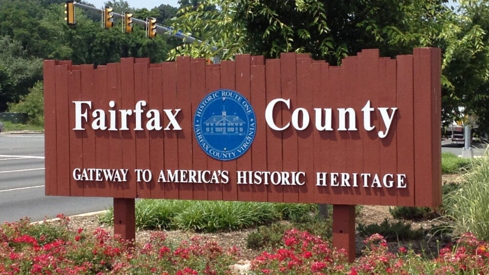 A large wooden Fairfax County sign with the seal of Fairfax County, Virginia, and the slogan Gateway to Americas Historic Heritage, stands by a roadside near flowers and greenery—highlighting local pride in water treatment Fairfax County initiatives.
