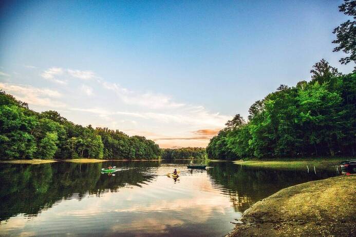 People kayak on a calm river surrounded by dense green trees under a blue sunset sky. The peaceful scene, much like reliable well pump services Howard County residents trust, reflects the beauty and tranquility of the outdoors.