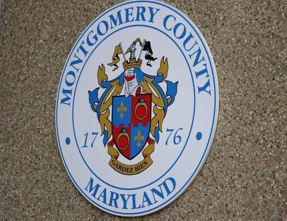 A round seal for Montgomery County, Maryland, featuring a colorful coat of arms, blue lettering, and the founding year 1776 against a textured beige wall—perfect for businesses like well pumps Montgomery County.