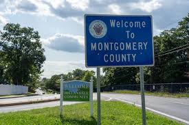 A blue road sign reads Welcome to Montgomery County beside a road, with trees and another green Welcome sign in the background on a sunny day, highlighting the area known for its reliable water treatment, Montgomery County MD.