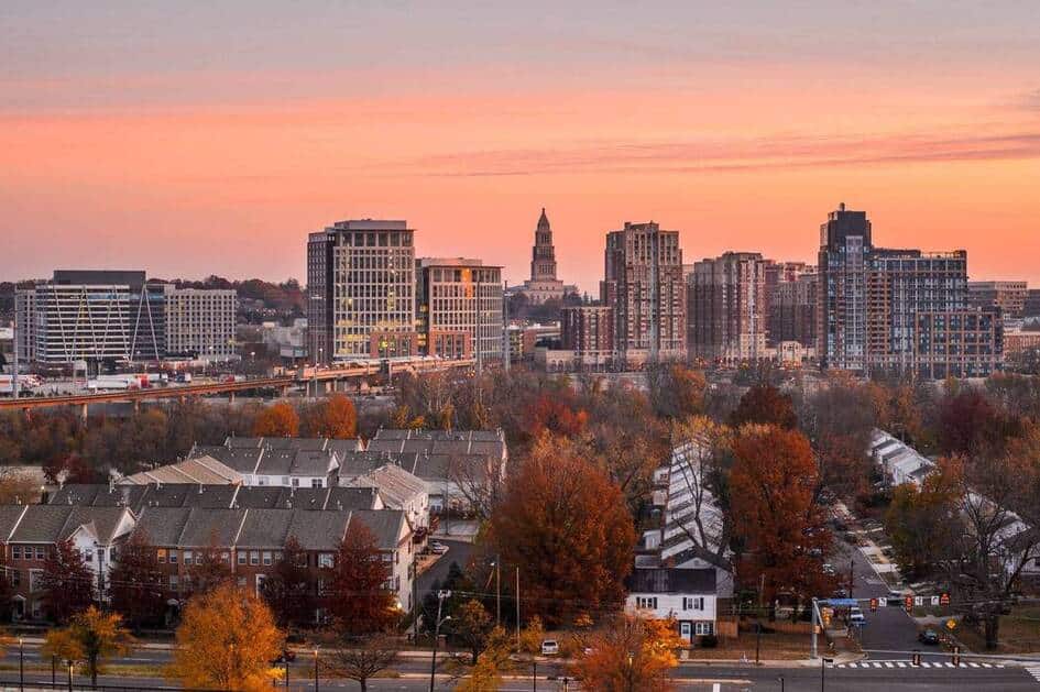 A view of a city skyline at sunset with modern high-rise buildings in the background and rows of residential houses near colorful autumn trees, highlighting the role of water treatment in Northern Virginia’s vibrant urban landscape.