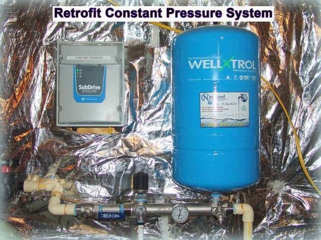 A Constant Pressure System for Well Water setup with a SubDrive utility controller on the left and a large blue Well-X-Trol pressure tank on the right, mounted against a reflective foil wall with connected pipes and gauges.